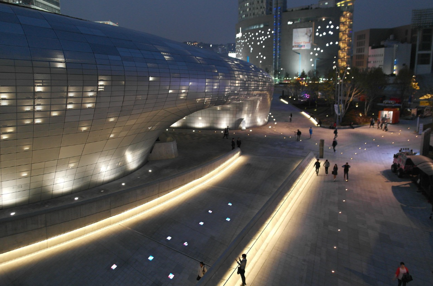 The futuristic Dongdaemun Design Plaza (DDP) in Seoul, glowing with dynamic lights. Its sleek, curvaceous architecture represents the "Unstoppable Trends of South Korea in 2026," symbolizing the intersection of "Wellness Wealth" and the next era of K-Culture.