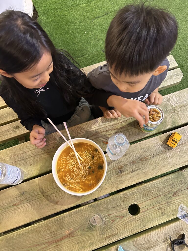 Seoul Travel Guide: Happy children enjoying freshly brewed Han River instant ramyeon at an outdoor riverside picnic table in Seoul.
