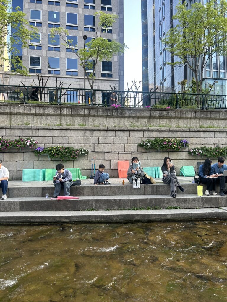 Seoul Travel Guide: Locals and international travelers reading books on fun-design chairs at the open-air Seoul Outdoor Library along Cheonggyecheon Stream.