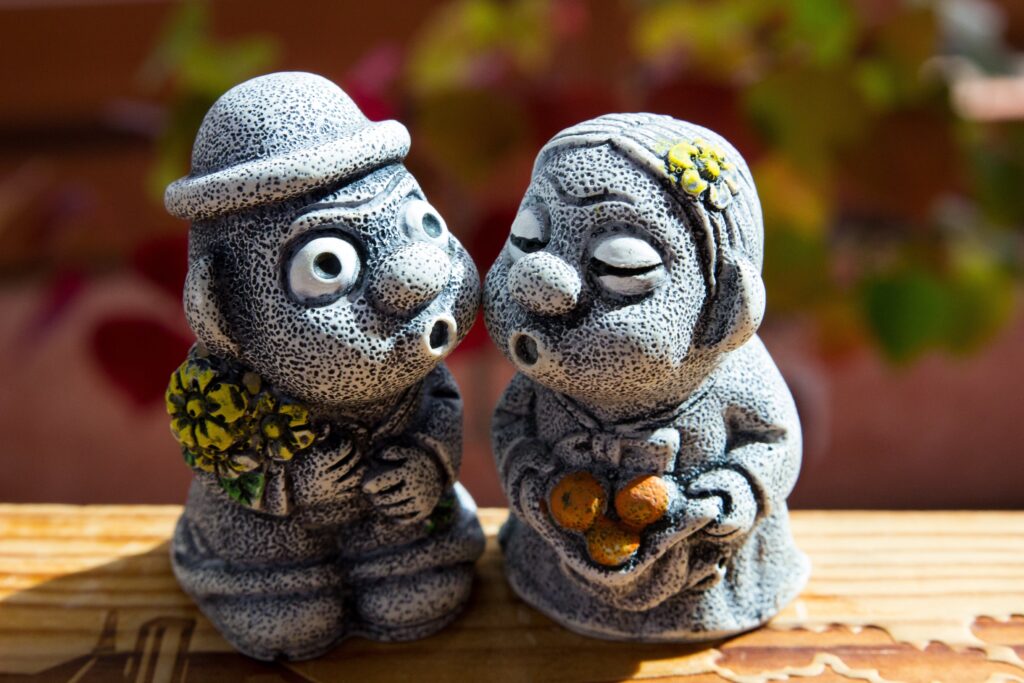 A traditional volcanic basalt stone statue known as Dolhareubang or Stone Grandfather on Jeju Island, surrounded by blooming orange orchards under a clear sky, representing the rustic 1950s background of the K-drama When Life Gives You Tangerines.