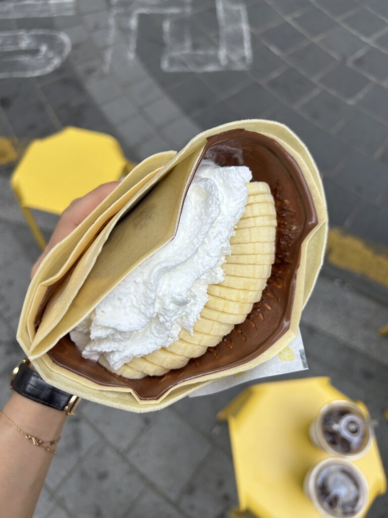 A close-up photograph of a delicious Nutella banana crepe wrapped in paper, freshly made from Deoksugung Cafe Doldam Kong near Deoksugung Palace.