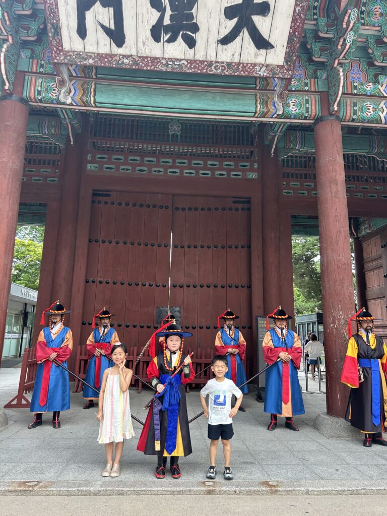 Children posing for a commemorative photo in front of the royal guards dressed in traditional Korean costumes during the Royal Guard Changing Ceremony at Deoksugung Palace.